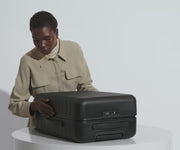 A female model filling The Bigger Carry-On suitcase in Jet Black with Away's packing organizers and using the interior organization and compression system for seamless packing