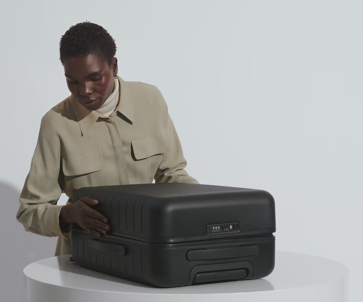 A female model filling The Bigger Carry-On suitcase in Jet Black with Away's packing organizers and using the interior organization and compression system for seamless packing